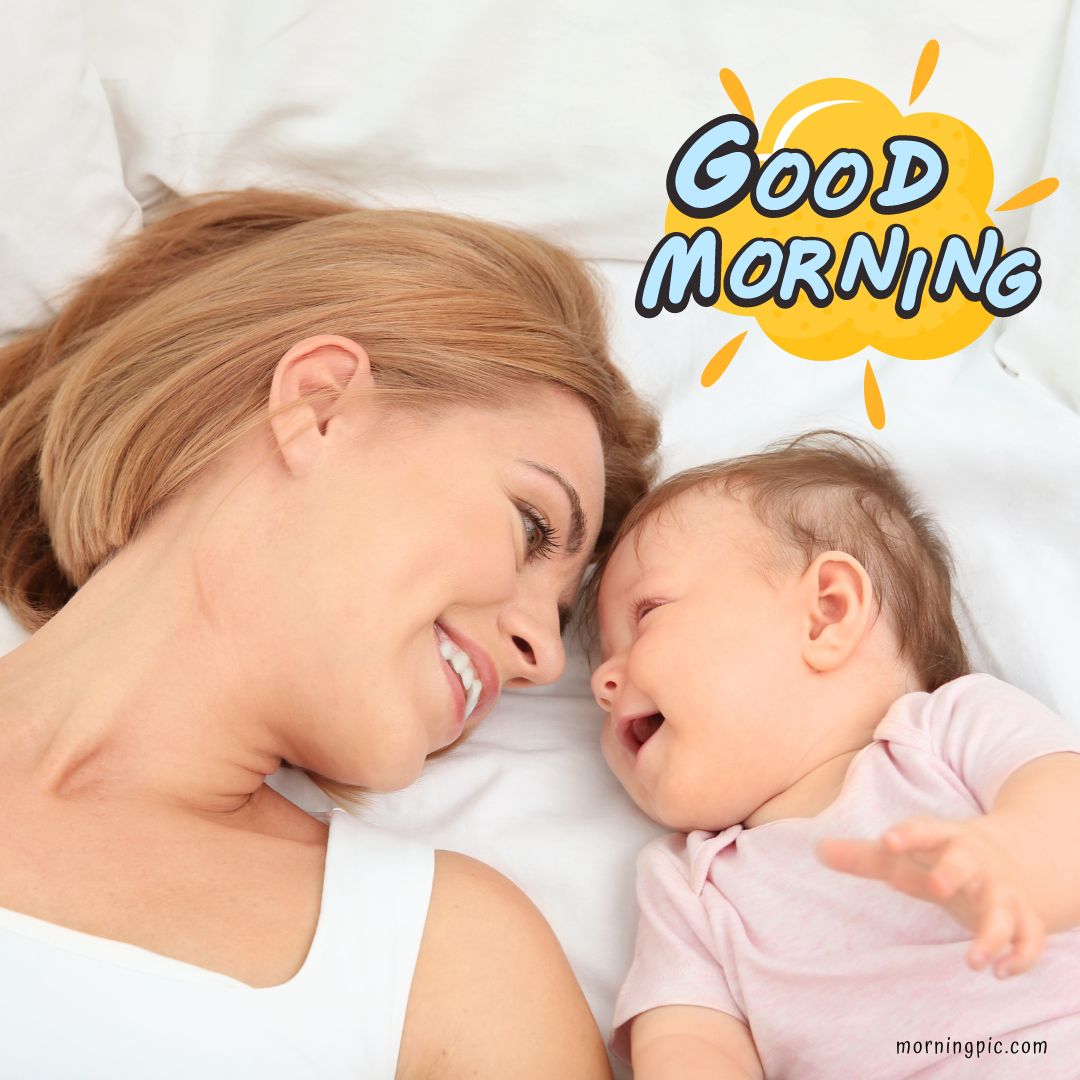 A smiling woman lies on a bed next to a baby girl who is also smiling and reaching out. Above them, the text "Good Morning Baby Girl" is written in cheerful, bold letters with a sun illustration.