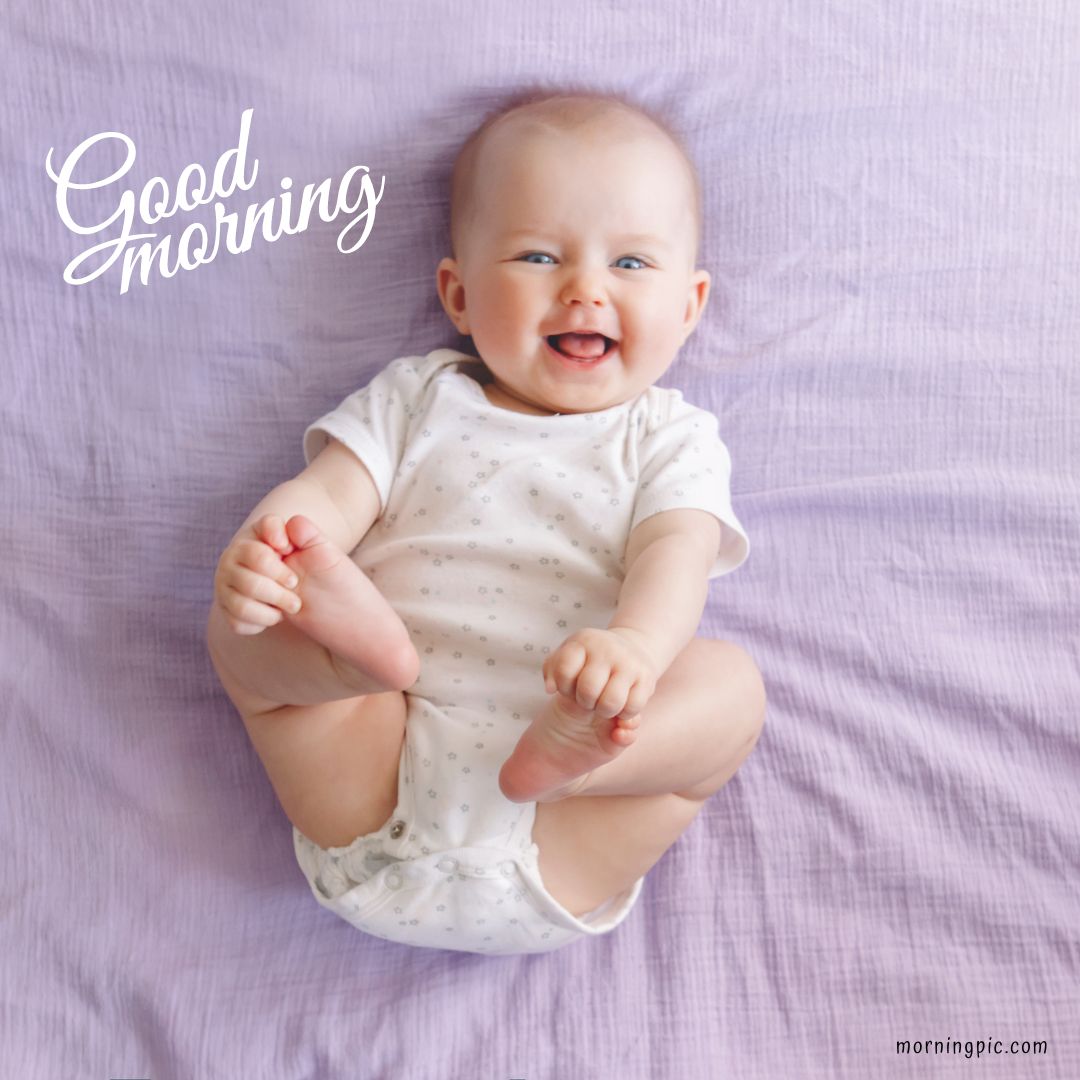 A happy baby, wearing a white onesie, lies on a lavender blanket. The baby is smiling and reaching for their feet. The text "Good Morning Baby Images" is written in white cursive in the top left corner. 