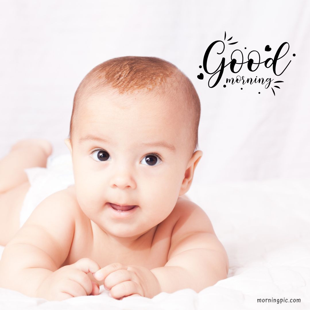 A baby girl lying on a white blanket, looking at the camera with wide eyes and a slight smile. The text "Good morning" is written in a decorative font near the top-right corner of the image.