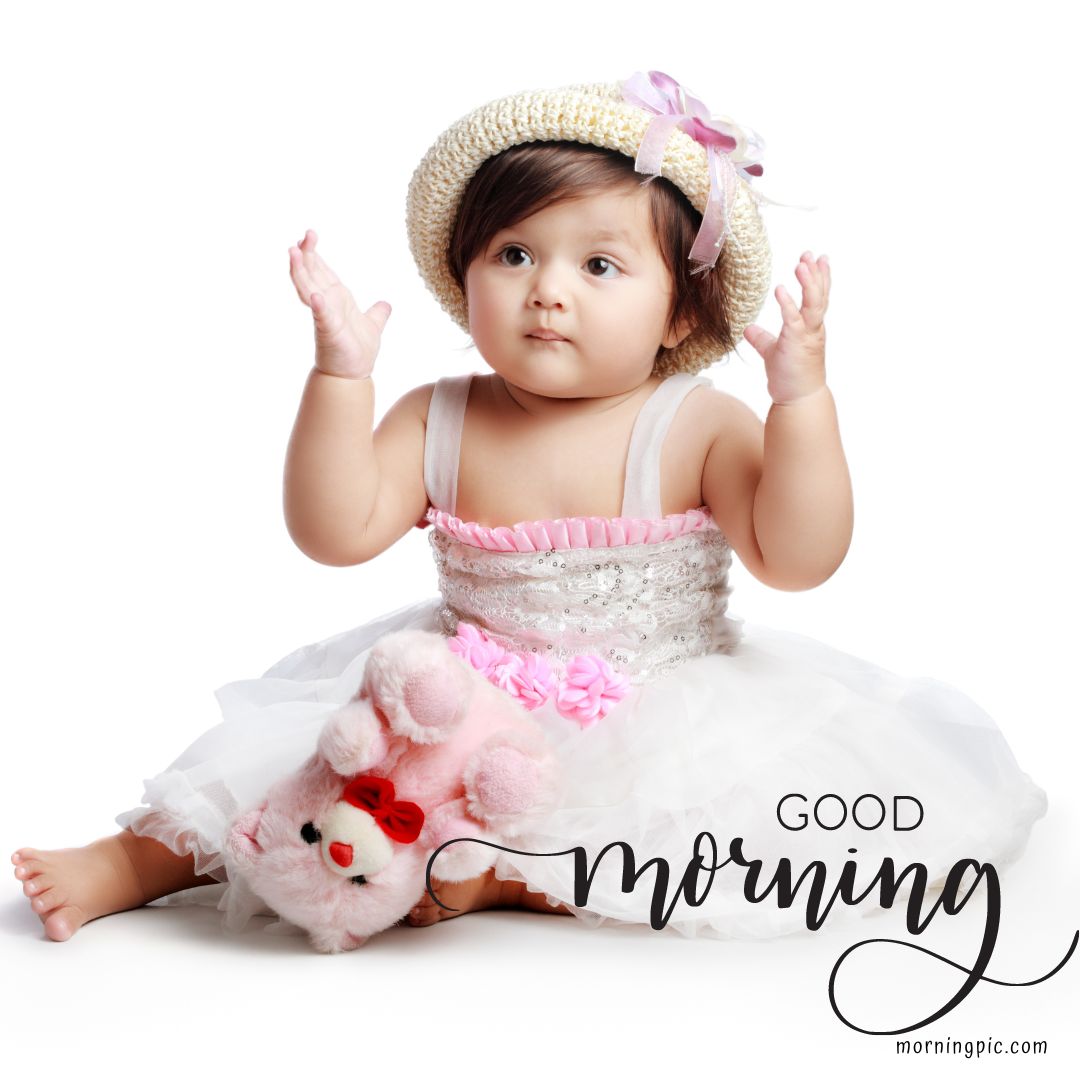 A baby wearing a white and pink dress and a straw hat is sitting on the floor with their hands raised. A pink stuffed bear rests on their lap. "Good Morning Baby Images HD" is written in script on the bottom right. The background is white.