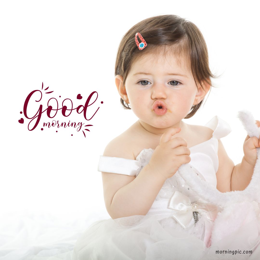 A baby girl with short dark hair, wearing a white dress, is holding a stuffed animal and making a cute face with her lips puckered. The text "Good Morning Baby Girl" is written stylishly on the left side.