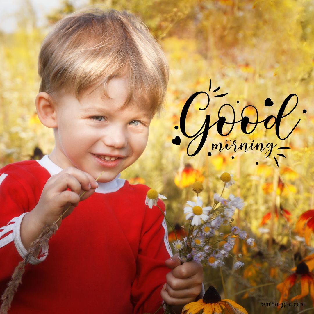 A young child with blonde hair, wearing a red and white outfit, smiles while holding a bouquet of wildflowers. The background is a field of flowers, and the text "Good Morning Baby Girl" is written in a whimsical font on the right side of the image. The image has a warm, sunny ambiance.