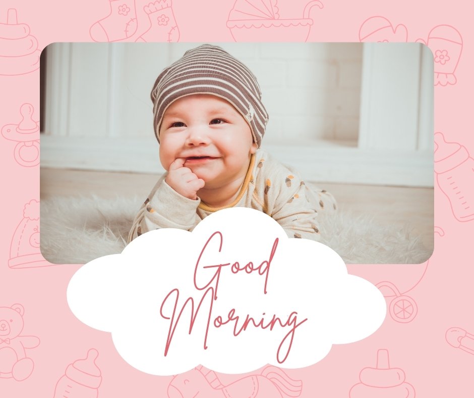 A smiling baby wearing a striped hat and beige outfit lies on a soft, fluffy surface. The pink background features baby-related icons like bottles and teddy bears. A white cloud shape in the foreground has "Good Morning" written in red cursive text. Perfect for Good Morning Baby Girl images.