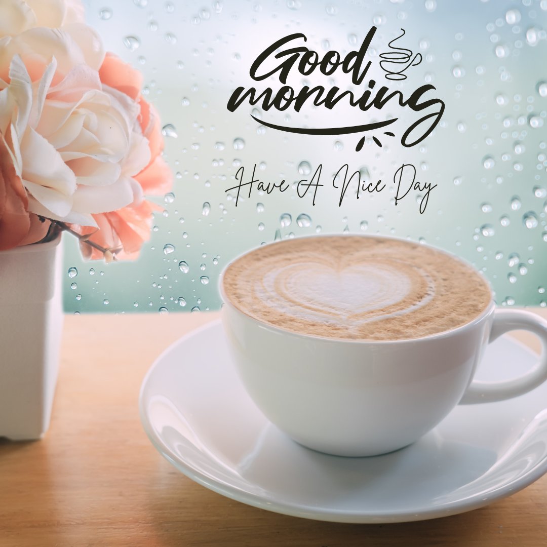 A cup of coffee with heart-shaped latte art sits on a white saucer on a wooden surface. Beside it is a white vase with pink and white flowers. The background features a rain-soaked window with the text "Good morning, Have A Nice Day." Perfect for sending Good morning Have a Nice day Images!