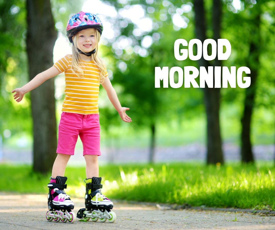 Good Morning Baby Images of a joyful young girl in a striped yellow shirt and pink shorts, balancing on rollerblades in a lush green park, with a bold 'Good Morning' text above.