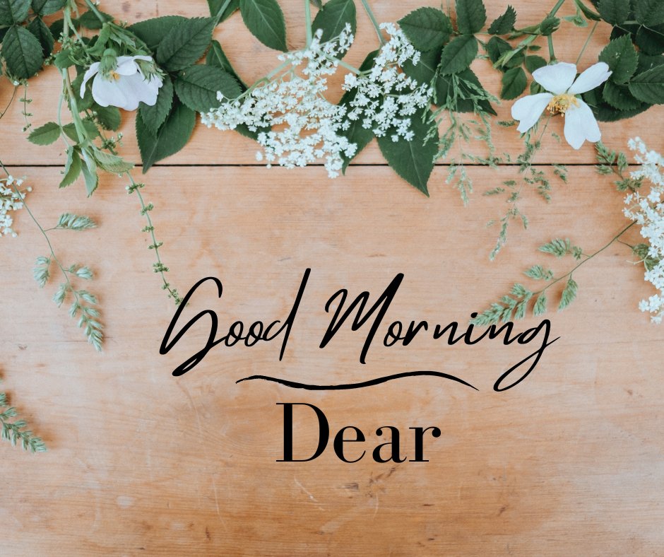 Good morning dear image featuring a serene display of fresh spring flowers and green leaves artistically arranged on a wooden surface, conveying a peaceful and natural morning greeting.