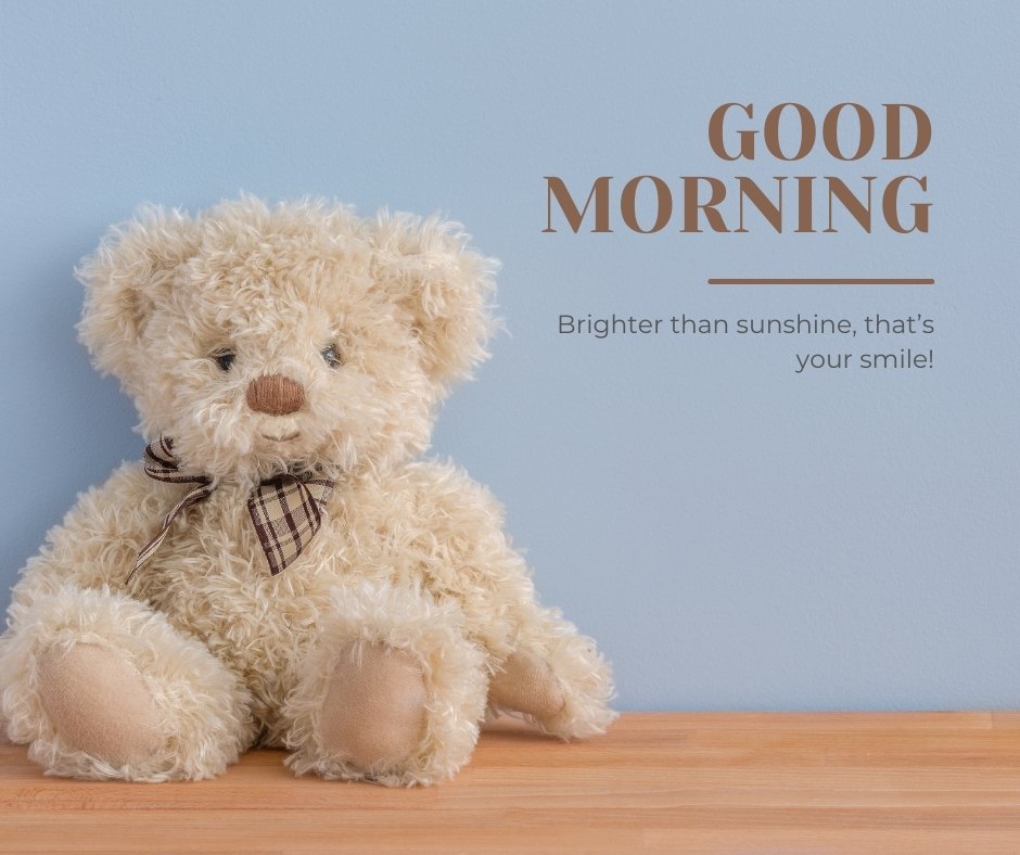 A fluffy light beige teddy bear seated against a light blue wall, featuring the caption "Good Morning: Brighter than sunshine, that’s your smile!" This charming image radiates warmth and positivity, ideal for a morning greeting.